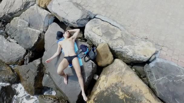 Joven hombre atlético sin camisa sentado en la roca por el mar — Vídeo de stock