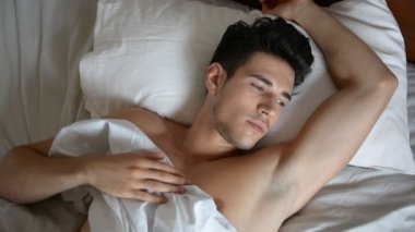 Tişörtsüz seksi erkek model yatağında tek başına yatıyor.