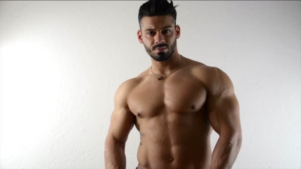 Gespierde bodybuilder door witte muur — Stockvideo