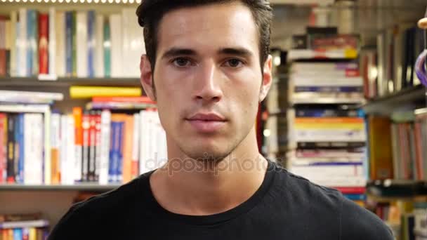 Красивый молодой человек в книжном магазине улыбается — стоковое видео