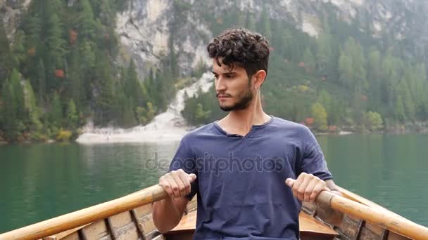 Молодий чоловік веслує на човні на гірському озері — стокове відео