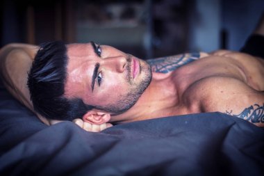Tişörtsüz seksi erkek model yatağında tek başına yatıyor.