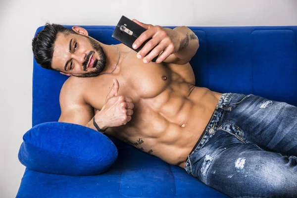 Male bodybuilder taking selfie photo on sofa — Stock Photo, Image