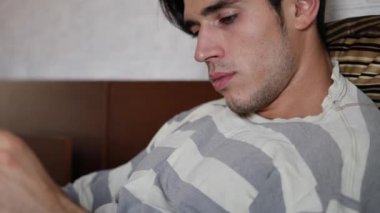 Genç adam yatakta uzanıp kitap okuyor.