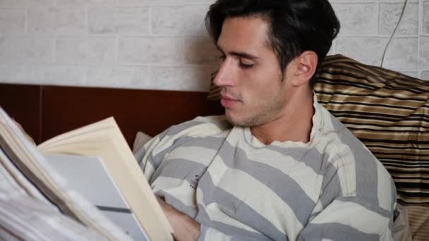 Joven acostado en la cama leyendo un libro — Vídeos de Stock