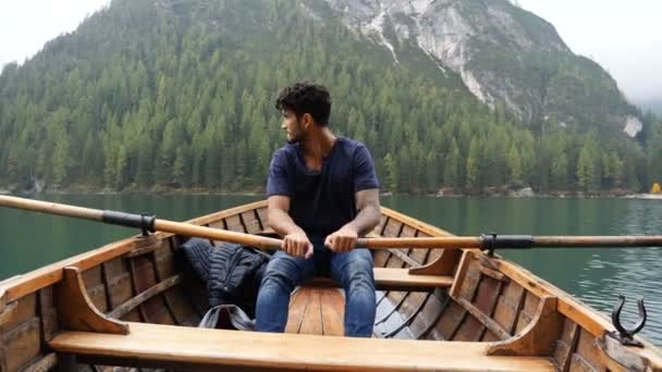 Молодий чоловік веслує на човні на гірському озері — стокове відео