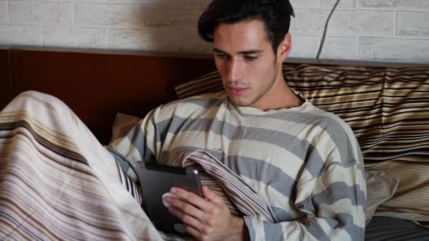 Guapo joven en la cama escribiendo en la tableta PC — Vídeos de Stock