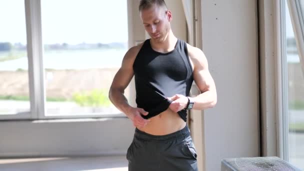 Молодой человек надевает рубашку на обнаженный мускулистый торс — стоковое видео