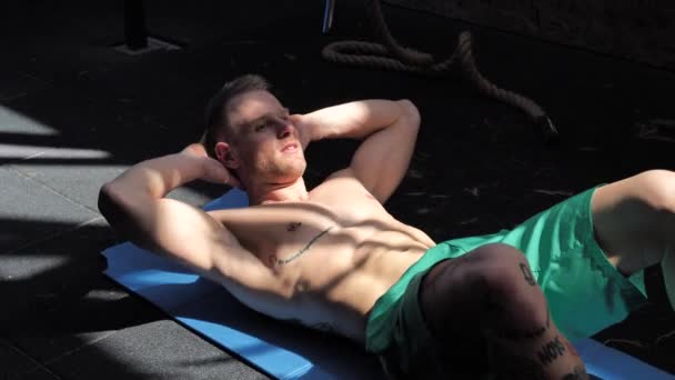 Przystojny młody człowiek robi ćwiczenia brzucha na macie — Wideo stockowe