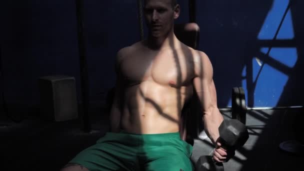 Muscular jovem sem camisa, treinando bíceps no banco de ginástica — Vídeo de Stock