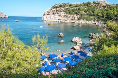 Anthony Quinn 'de turist, şemsiye ve güneş sandalyeli küçük plaj (Rodos, Yunanistan)