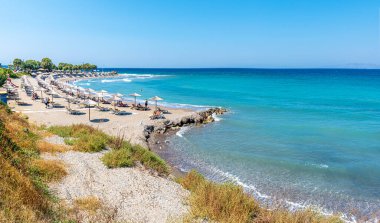 Kamiros yakınlarında insanlar, şemsiyeler ve güneşliklerle plaj (Rodos, Yunanistan)