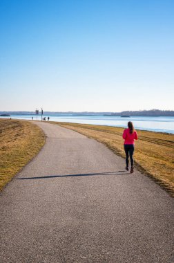 Genç kız asfaltta koşuyor güneşli bir günde Gabcikovo Barajı 'nın kıyısında yürüyor    