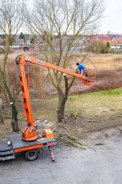 Zincirli testereyle ağaç dallarını budama platformunda bir adam var. 