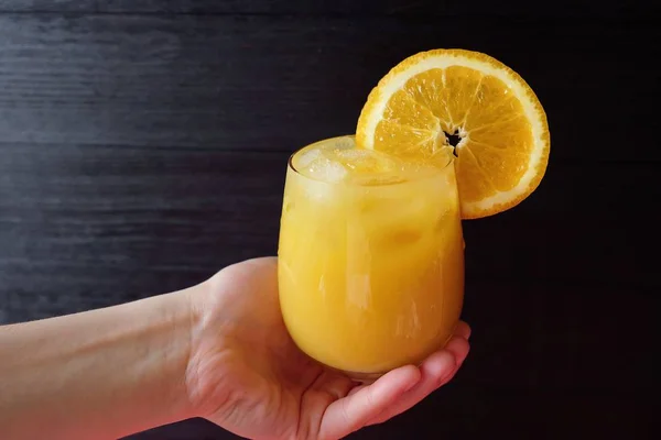 Χυμό πορτοκάλι στο χέρι σε σκούρο φόντο — Φωτογραφία Αρχείου