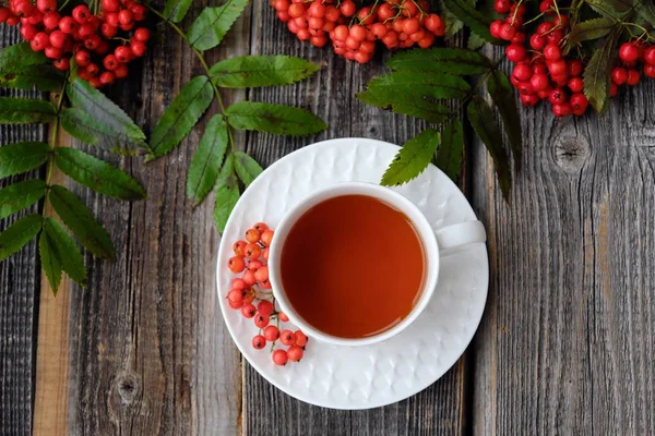 Вкусная чашка чая и ягод роуэн на деревянном столе — стоковое фото