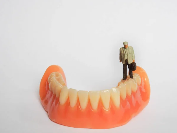 Miniature elderly standing on removable denture, on white backgr — Stock Photo, Image