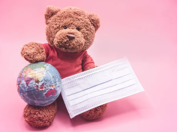 Brown teddy bear wearing a surgical mask protects against coronavirus, holding the earth globe. Campaign to put on a mask to reduce the spread of coronavirus. Hygiene and Healthcare concept