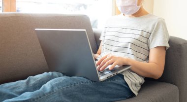 Güzel Asyalı kadınlar, Coronavirus salgını sırasında evlerinde internet ekibiyle konferans yapmak için dizüstü bilgisayar kullanarak oturma odasındaki kanepede rahatça oturuyorlar. Ev kavramından çalış.