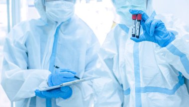 Korunma giysisi giymiş Asyalı kadın doktor karantina hasta dosyasında maske yazıyor. Koronavirüs taraması için kan örneğiyle birlikte test tüpü tutuyor. Coronavirus, covid-19 konsepti.