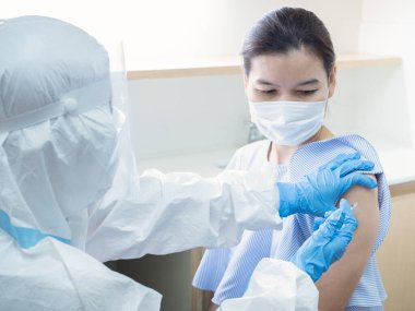 Kişisel koruyucu giysili Asyalı kadın doktor, Coronavirus enfeksiyonu riski olan güzel kadın hastaların bağışıklığını arttırmak için aşı yapıyor. Coronavirus, covid-19 ve aşı konsepti.