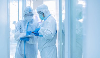 Korunma giysisi giymiş Asyalı kadın doktor karantina hasta dosyasında maske yazıyor. Koronavirüs taraması için kan örneğiyle birlikte test tüpü tutuyor. Coronavirus, covid-19 konsepti.