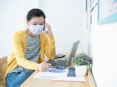Maske takan güzel Asyalı kadınlar Coronavirus 'un yayılmasını önlemek için evde defter, tablet ve akıllı telefon kullanıyorlar. Evden çalışma, sosyal uzaklık, covid-19 ve coronavirüs konsepti.