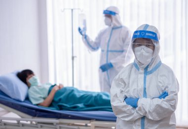 İki Asyalı doktor N95 maskeli ve yüz kalkanlı PPE kıyafeti giyer, koronavirüs enfeksiyonlu hastayı negatif basınç odasında tedavi eder ve kullanır. Coronavirus, tıbbi ve covid19 konsepti.