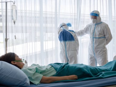 İki Asyalı doktor N95 maskeli ve yüz zırhlı PPE giyiyorlar. Negatif basınç odasında 19 hastayı tedavi ederken yorgun ve depresif hissediyorlar. Coronavirus ve tıbbi konsept.