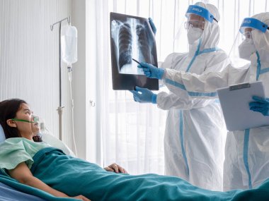 İki Asyalı doktor N95 maskeli ve yüz bakımlı PPE kıyafeti giyer. Negatif basınç odasındaki koronavirüs enfeksiyonlu hastanın göğüs röntgenini incelerler. Coronavirus, tıbbi ve covid19 konsepti