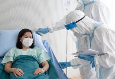 İki doktor yüz maskeli PPE kıyafeti giyer, koronavirüsün vücut ısısını ölçer ve negatif basınç karantina odasında kızılötesi termometre tabancasıyla hasta enfekte eder. Tıbbi ve covid19 konsepti