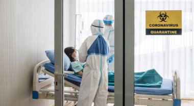 İki Asyalı doktor N95 maskeli ve yüz kalkanlı PPE kıyafeti giyer, koronavirüs enfeksiyonlu hastayı negatif basınç odasında tedavi eder, karantina uyarısı alan işareti ile etiketlenir. Coronavirus ve covid19 konsepti.