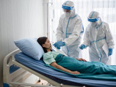 İki Asyalı doktor N95 maskeli PPE kıyafeti giyer ve yüz bakımı yapar, koronavirüslü oksijen maskesini negatif basınç odasında tedavi eder ve kullanır. Coronavirus, tıbbi ve covid19 konsepti.