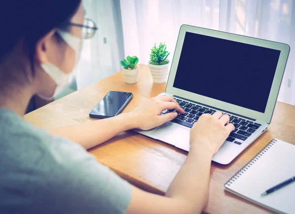 Asian women wearing masks work at home using notebook and smartphone to reduce spreading of coronavirus. Covid-19, work from home and social distancing concept. Vintage style with noise.