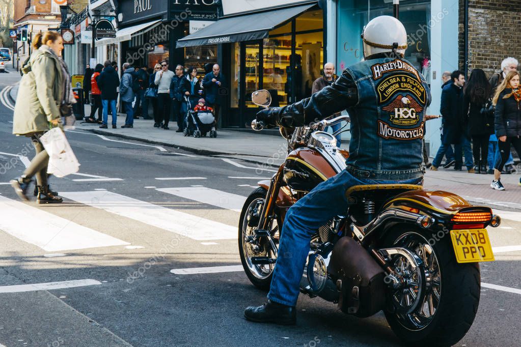 LONDON, UK - MARCH 13, 2016: Man on a Harley Davidson motorcycle with matching logo denim jacket wait for pedestrian crossing a road in Hampstead, London.