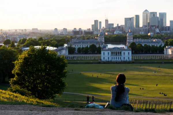 Woman sitting on the ground watching sunset over London skyline — Stock Photo, Image
