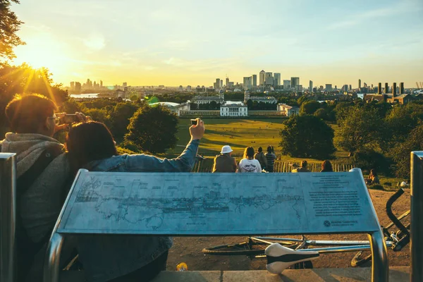 Pessoas sentadas no topo da colina em Greenwich Park, Londres, assistindo ao pôr do sol e tirando fotos . — Fotografia de Stock