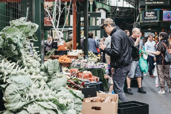 Hombre mirando las verduras en un puesto de mercado en Borough Market, Londres —  Fotos de Stock