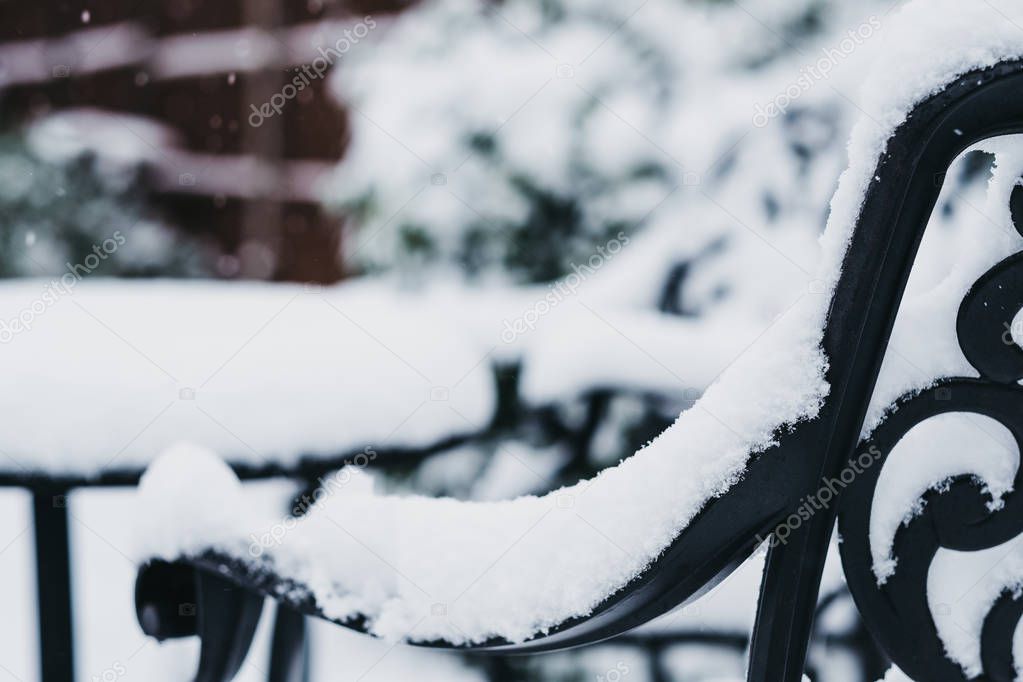 Close up of a black metal garden furniture in a garden in winter, covered in snow, snowing, selective focus. 