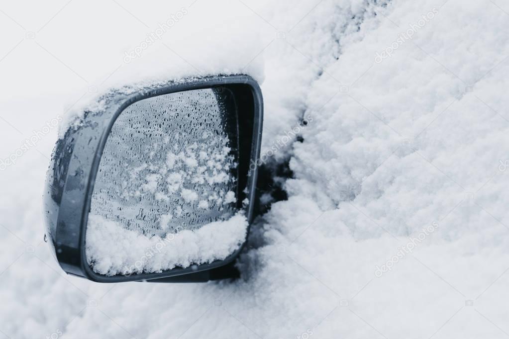 Side mirror on a car completely covered in snow, selective focus  