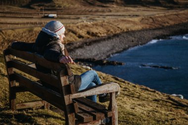 Adam ahşap Bank güneşli bahar gününde Isle of için gökyüzü, İskoçya, su üzerinde rahatlatıcı.