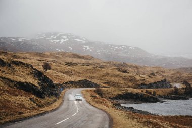 Kimliği belirsiz bir sisli bahar gününde İskoçya Highlands Lochinver yakınındaki geçmekte bir yolda araba.