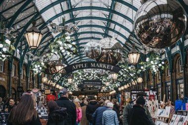 İnsanlar Apple Market tabelası ve Noel süslemeleri altında yürüyorlar