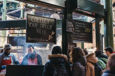 Londra, Uk - 29 Kasım 2019: Borough Market 'teki Northfield Butchery standında yemek bekleyen insanlar, arka planda yemek pişiren personel. Borough Market Londra 'nın en büyük pazarlarından biridir, Uk..