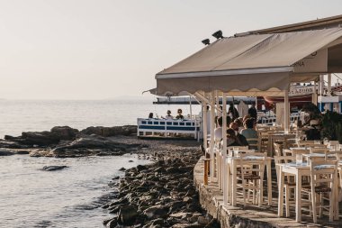 Hora, Mykonos - 23 Eylül 2019: Adanın başkenti Hora 'daki (Mykonos Town) eski liman kıyısındaki sahil restoranındaki insanlar, günbatımında Kiklad mimarisinin en iyi örneklerinden biri.