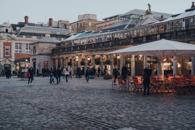 Londra, İngiltere - 06 Mart 2020: Covent Garden Market 'teki bir pazarın önündeki insanlar, alacakaranlıkta. Covent Garden, Londra 'da bir sürü dükkanı ve restoranı olan ünlü bir turizm alanıdır. Hareket bulanıklığı.