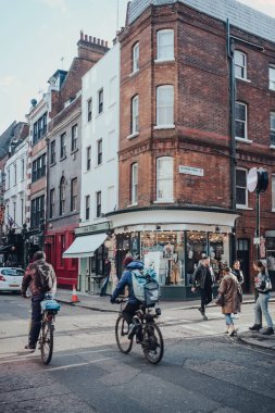Londra, İngiltere - Mart 06, 2020: Londra 'nın LGBTQ + barları, restoranları ve kulüpleriyle ünlü Soho' daki mağazalar ve kafeler, önde insanlar, bisikletçi ve Deliveroo motorcusu, hareket bulanıklığı.