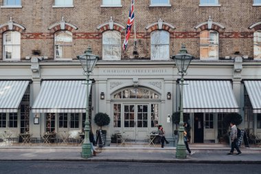 Londra, İngiltere - 6 Mart 2020: Soho 'daki Charlotte Street Hotel' in önünde sigara içen kadın, Londra 'nın barları, restoranları ve kafeleri ile ünlü bir bölge, güneşli bir bahar gününde, insanlar yanından geçer, hareket bulanıklığı.