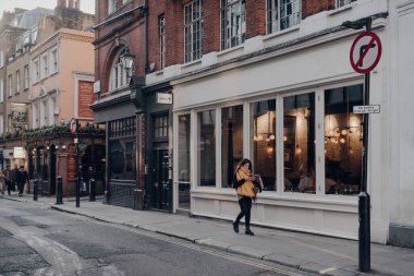 Londra, İngiltere - 06 Mart 2020: Soho 'daki kafeler ve restoranlar sırası, Londra' nın merkezindeki bar ve lokantalarla ünlü bir alan, önünden geçen kadın, hareket bulanıklığı.