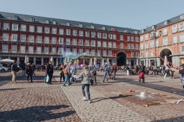 Madrid, İspanya - 26 Ocak 2020: İspanya 'nın zengin Avrupa sanat depolarıyla ünlü başkenti Madrid' in merkezindeki büyük bir kamusal alan olan Plaza Mayor 'da çocuklar sabun köpüklerini kovalıyor.
